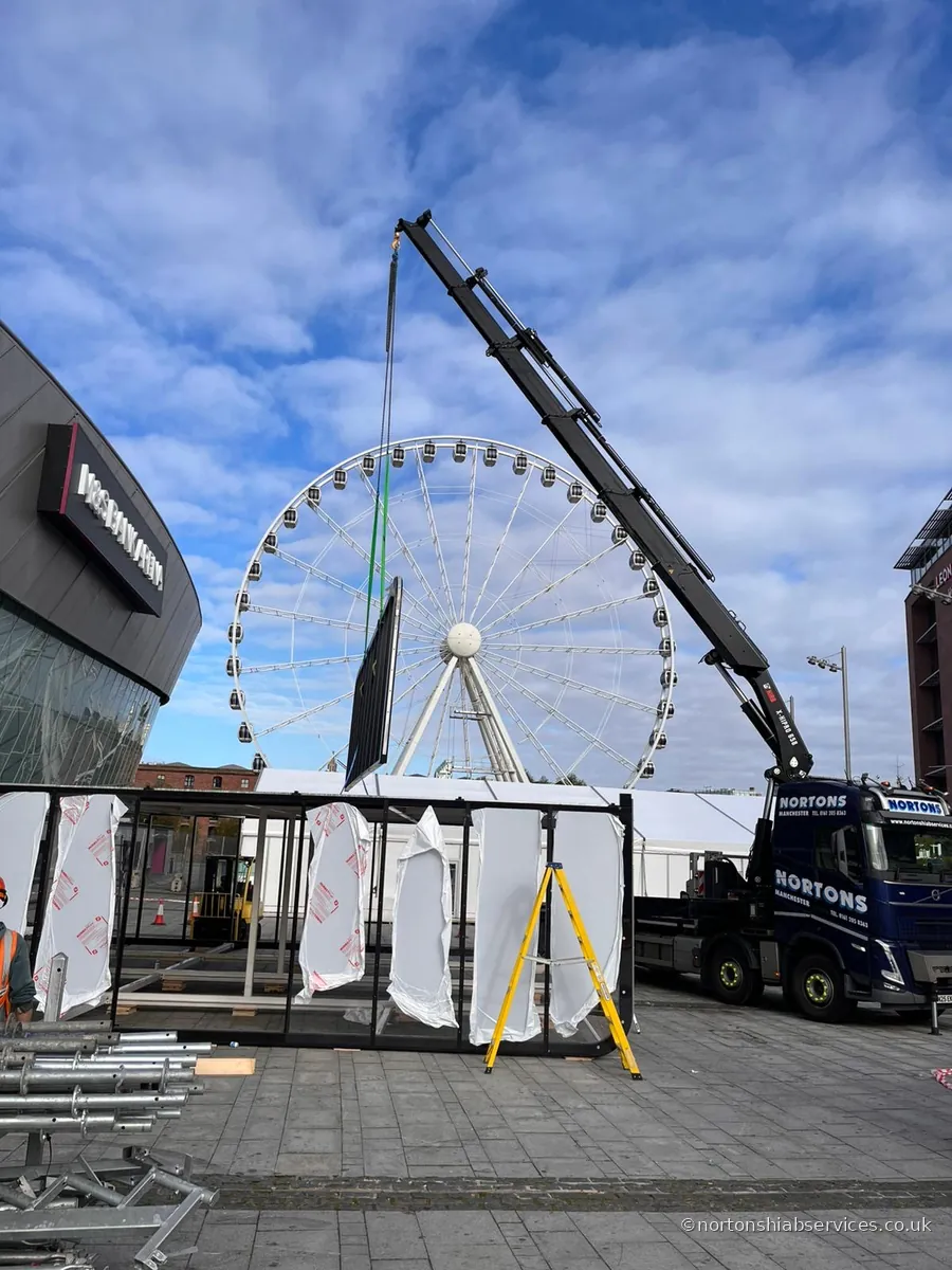 A Nortons lorry crane unloading panels on a waterfront beside a large observation wheel