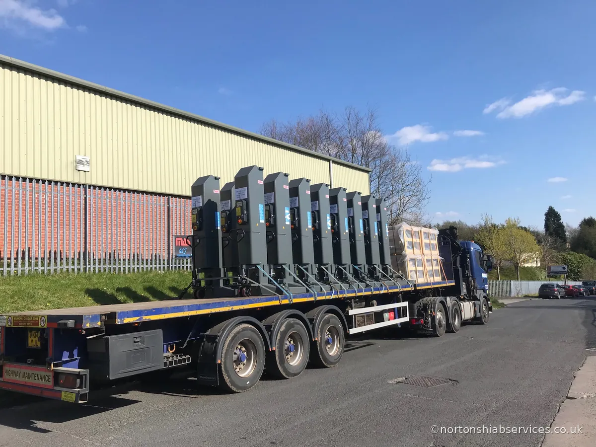 A Nortons trailer loaded with a row of dark stacked units outside a warehouse