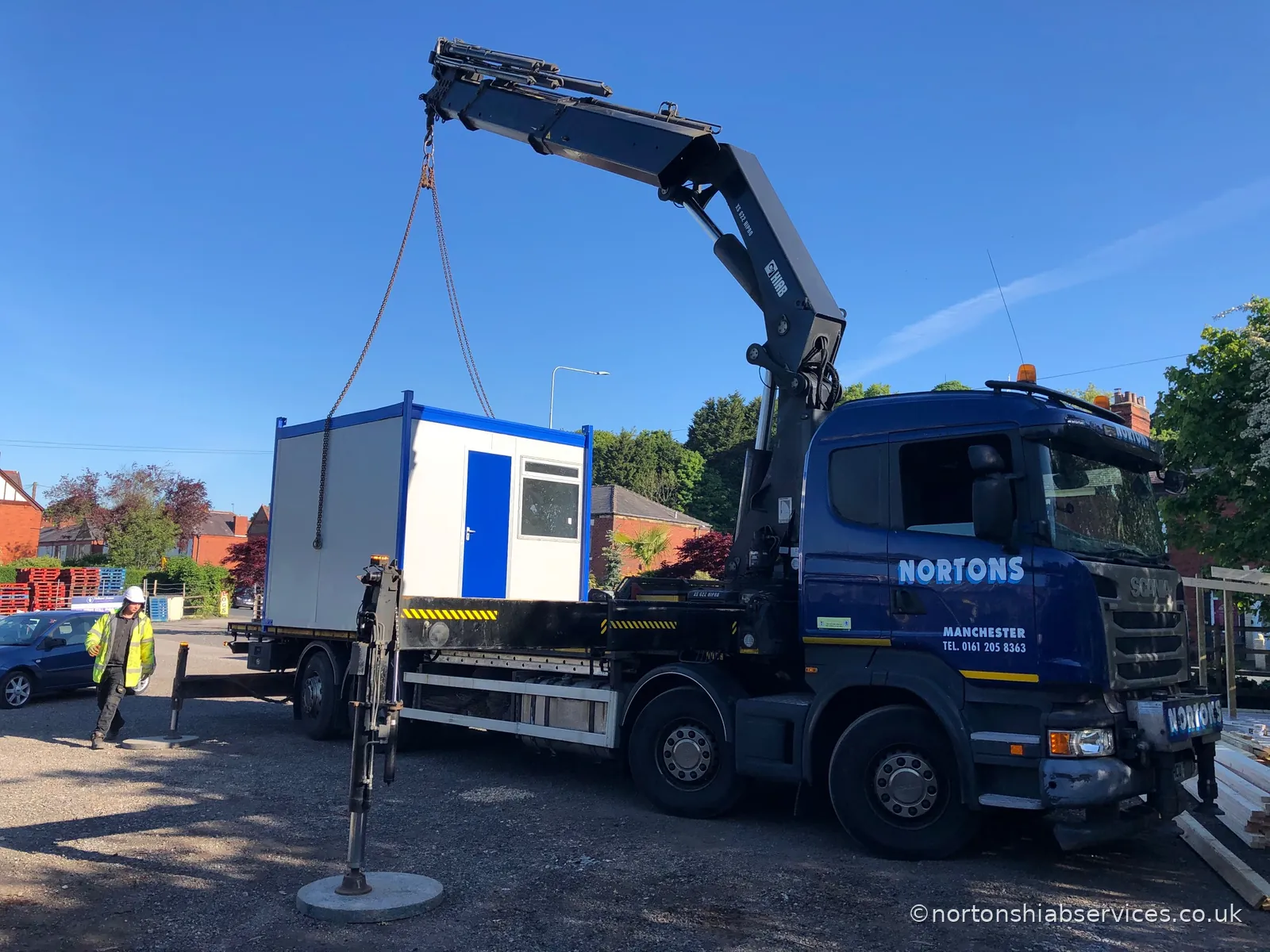 A Nortons rigid craning a blue and white nine foot portable cabin off the bed in a residential street