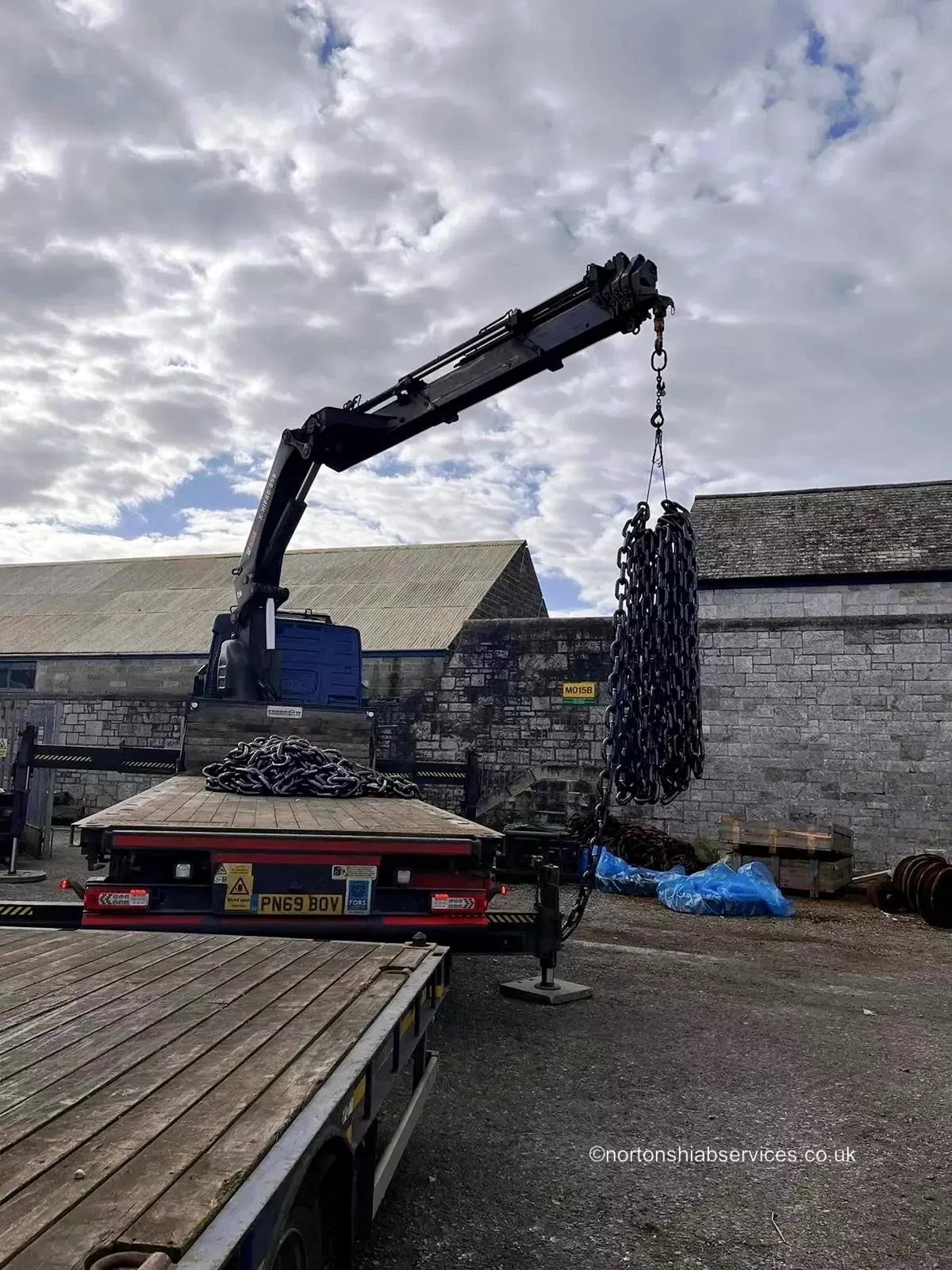 Nortons hiab lifting a heavy coil onto a flatbed using chains