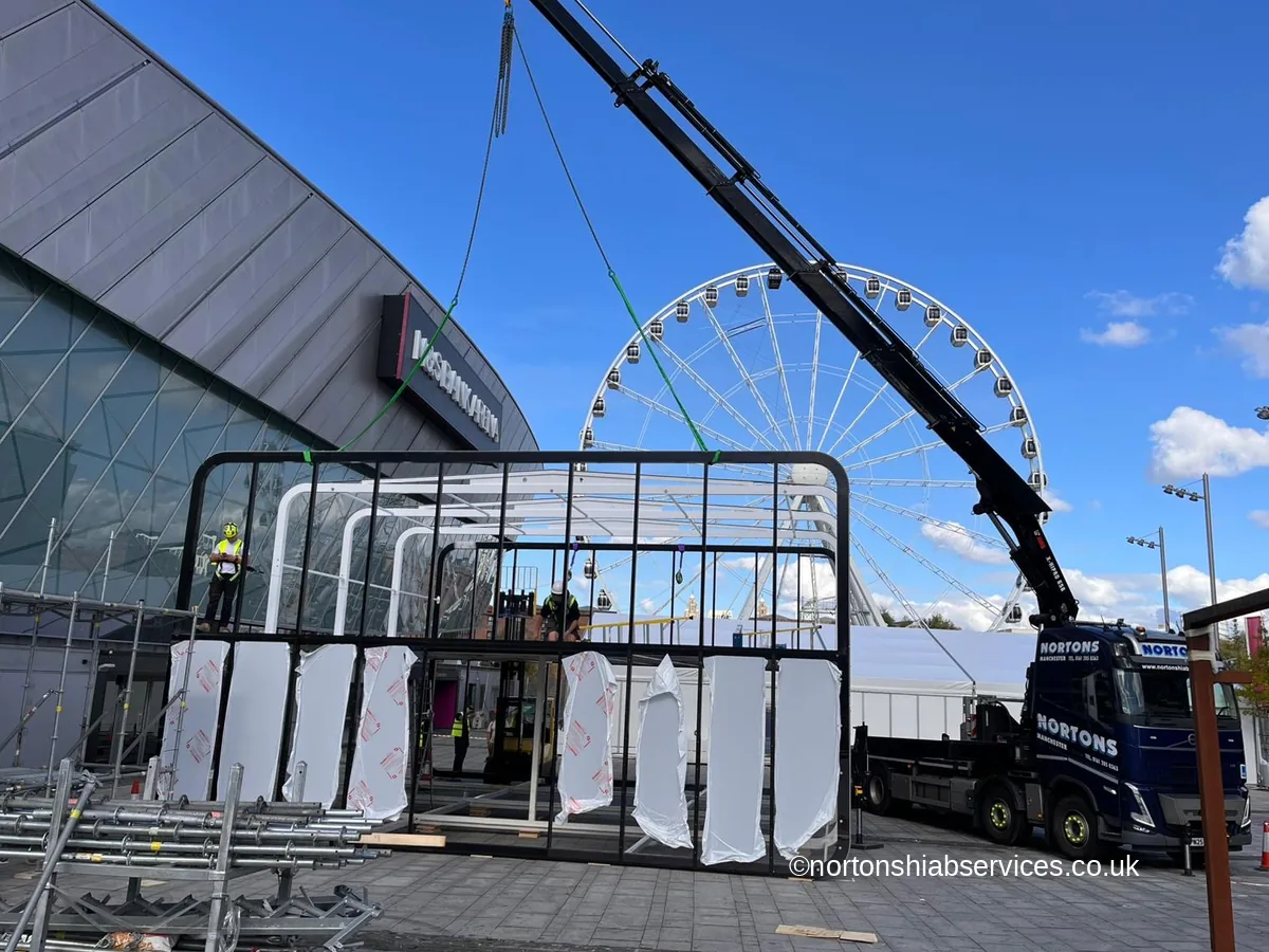 Nortons hiab reaching right across a public plaza to land a marquee frame, with the lorry standing well back at the far side