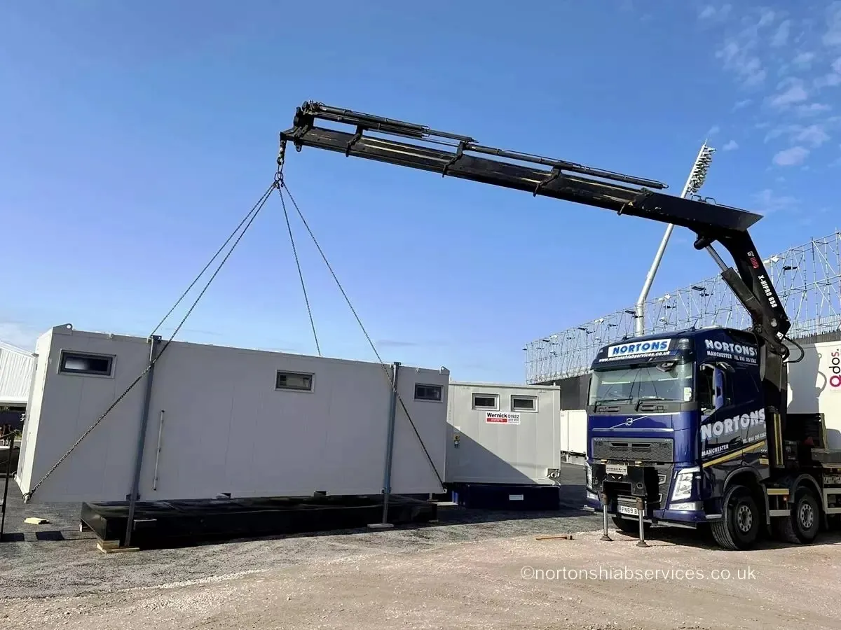 Nortons truck-mounted crane lifting a portable cabin on a spreader beam