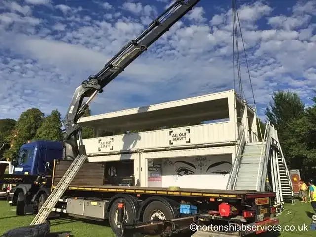 Nortons hiab lifting a container unit with a staircase onto the trailer at a festival site