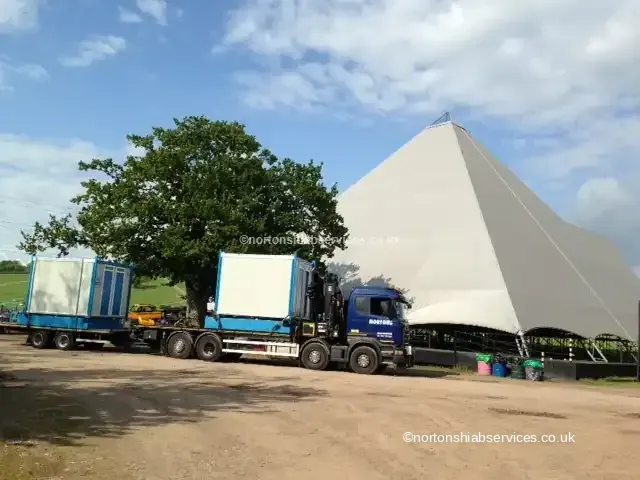 Two Nortons lorries loaded with site cabins standing beside the big tent at the Glastonbury festival site