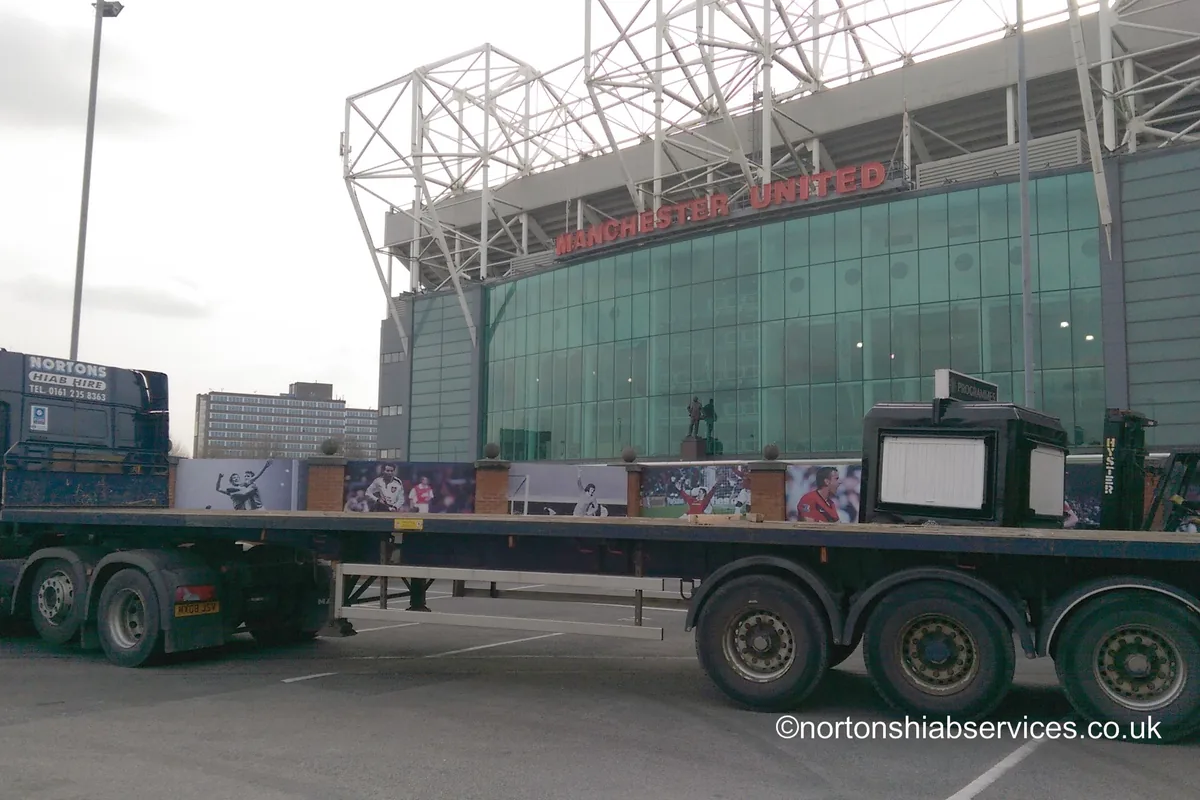 A Nortons tractor unit and flat trailer standing on the forecourt at Old Trafford below the Manchester United sign