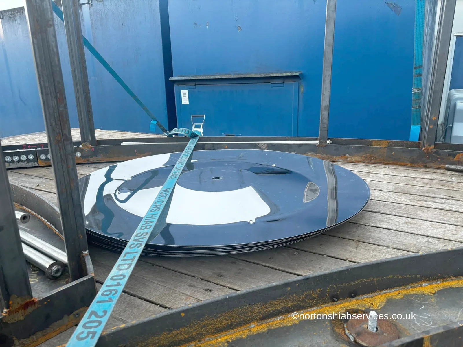 Mirror-finished discs from a giant tambourine stacked flat under a Nortons ratchet strap on the lorry deck