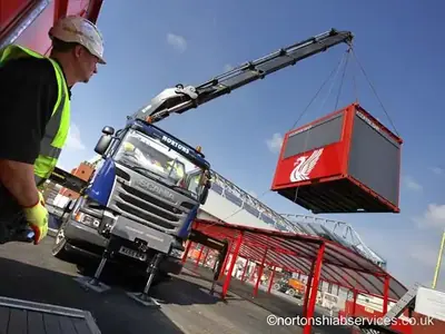 Red container unit lifted by a Nortons crane with a worker watching from the ground
