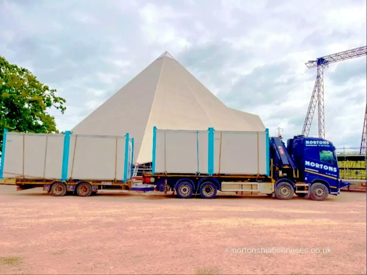 Nortons lorries loaded with site cabins beside a large marquee at the Glastonbury festival site