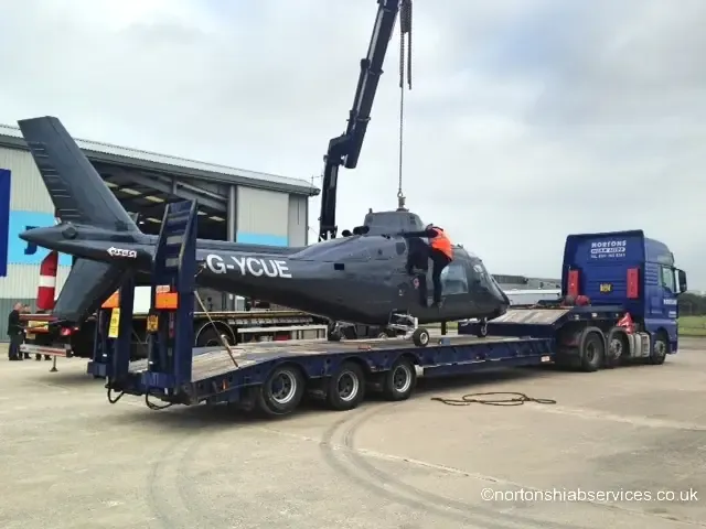 The helicopter with its main rotor blades removed, loaded and strapped on the Nortons low trailer outside the hangar at Blackpool Airport