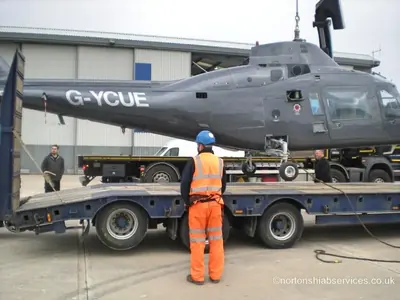 Helicopter landing gear settling onto the trailer deck with a banksman watching