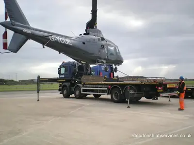 Helicopter airframe being lowered by crane towards a Nortons low trailer
