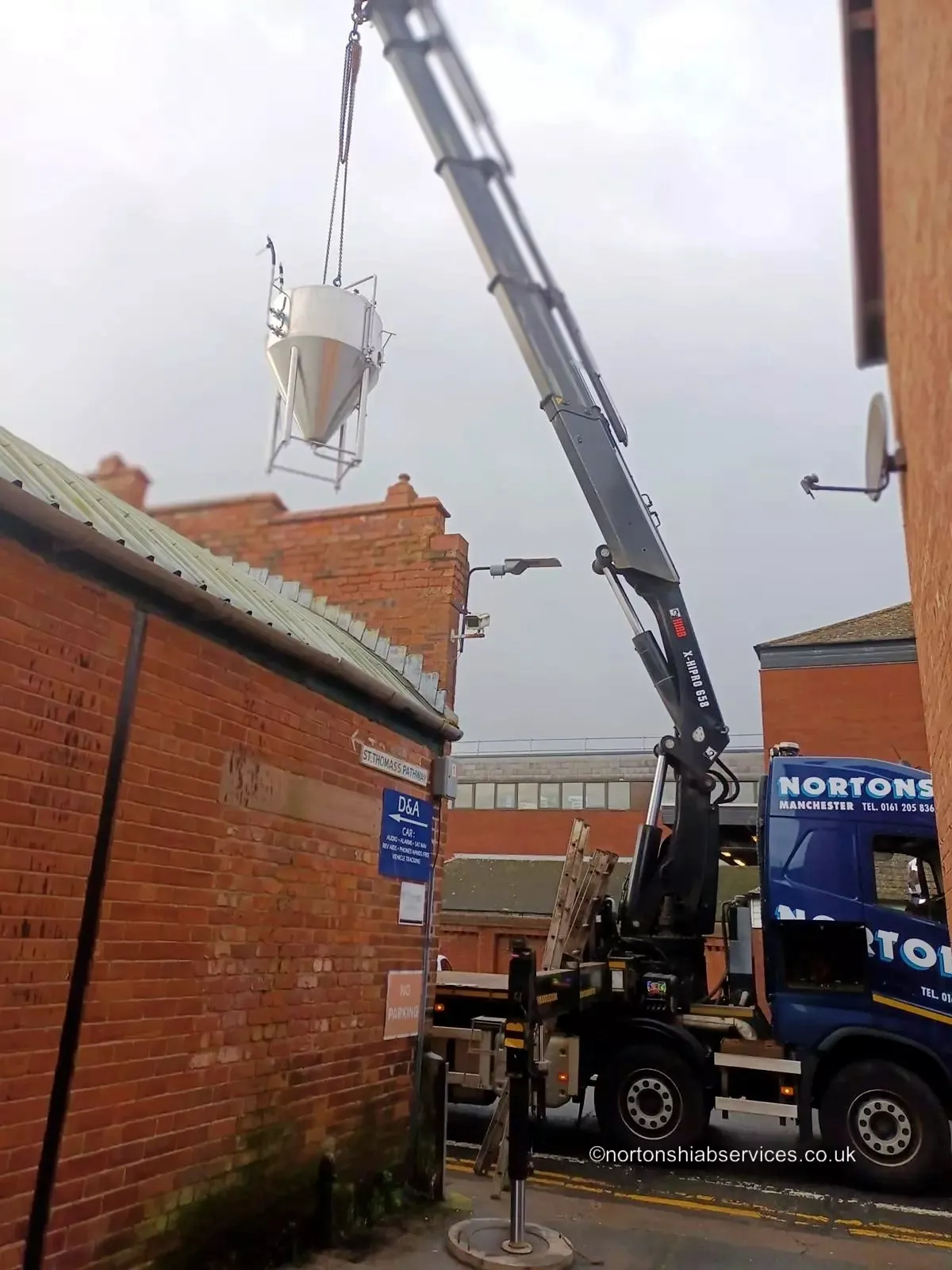 Nortons hiab crane lifting a load over a brick wall into a rear yard