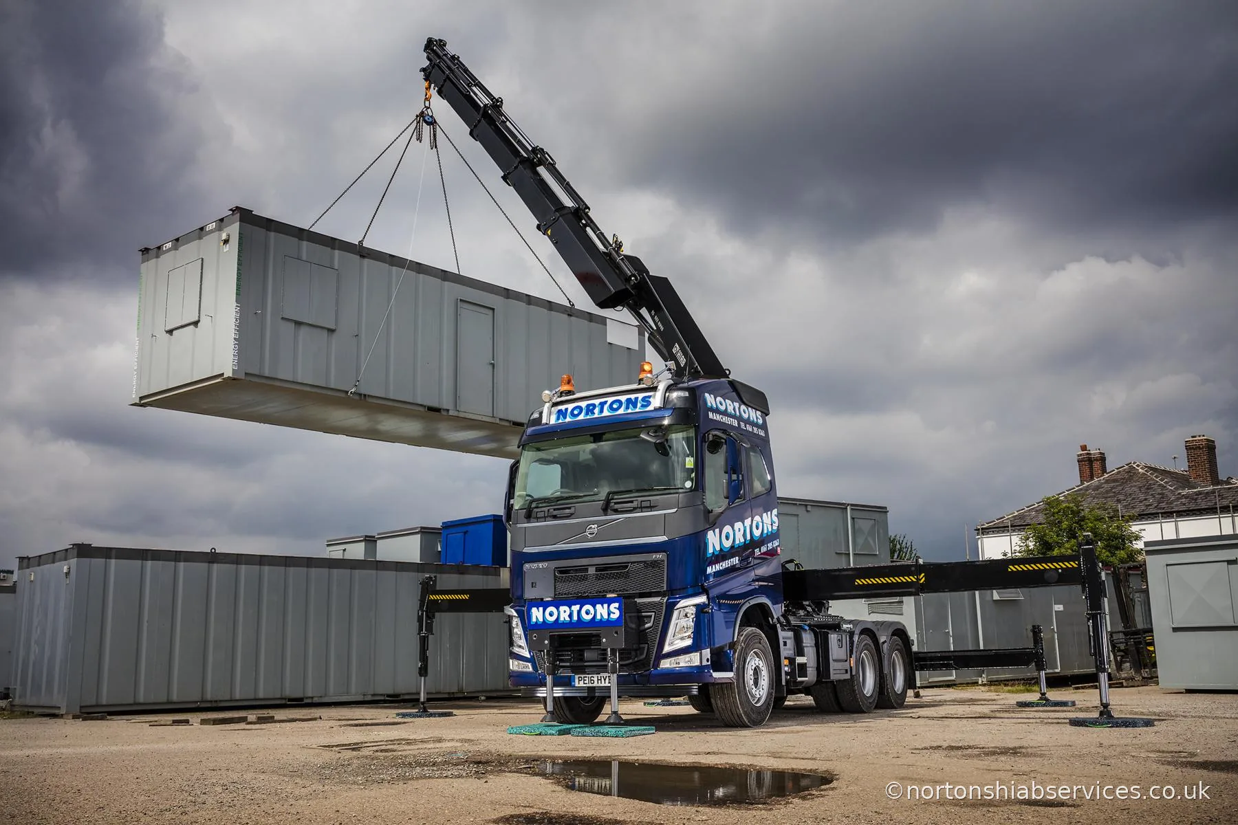 Nortons hiab crane-truck lifting a portable cabin off its trailer