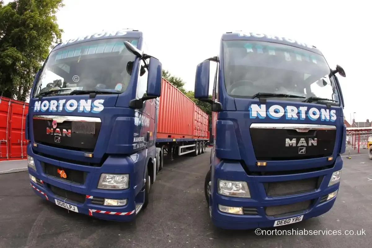 Two Nortons MAN tractor units standing nose to nose beside the red site containers at Anfield