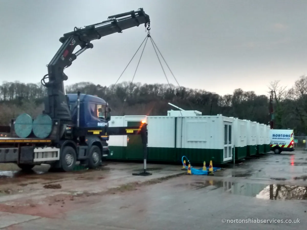 A Nortons hiab setting out green and white welfare cabins at a compound at Caernarfon