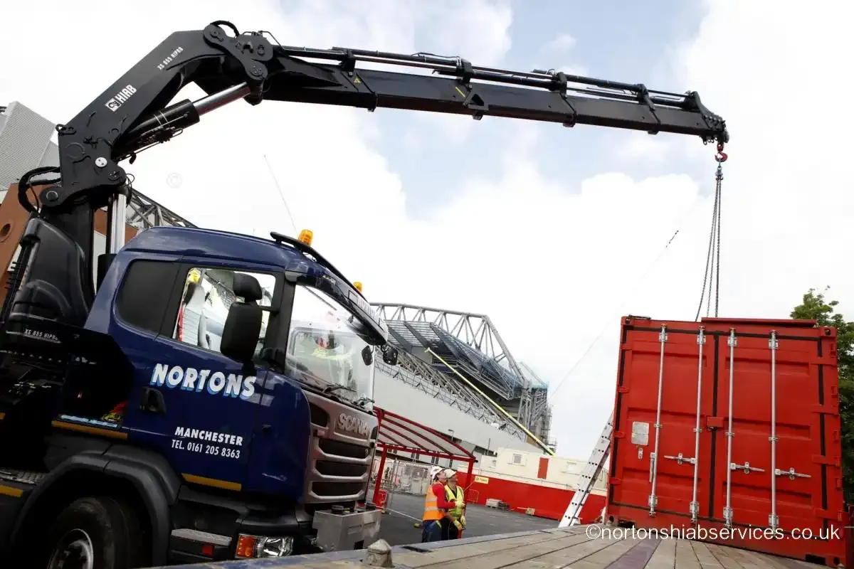 A Nortons rigid with its crane extended beside red site containers at the Anfield stadium compound
