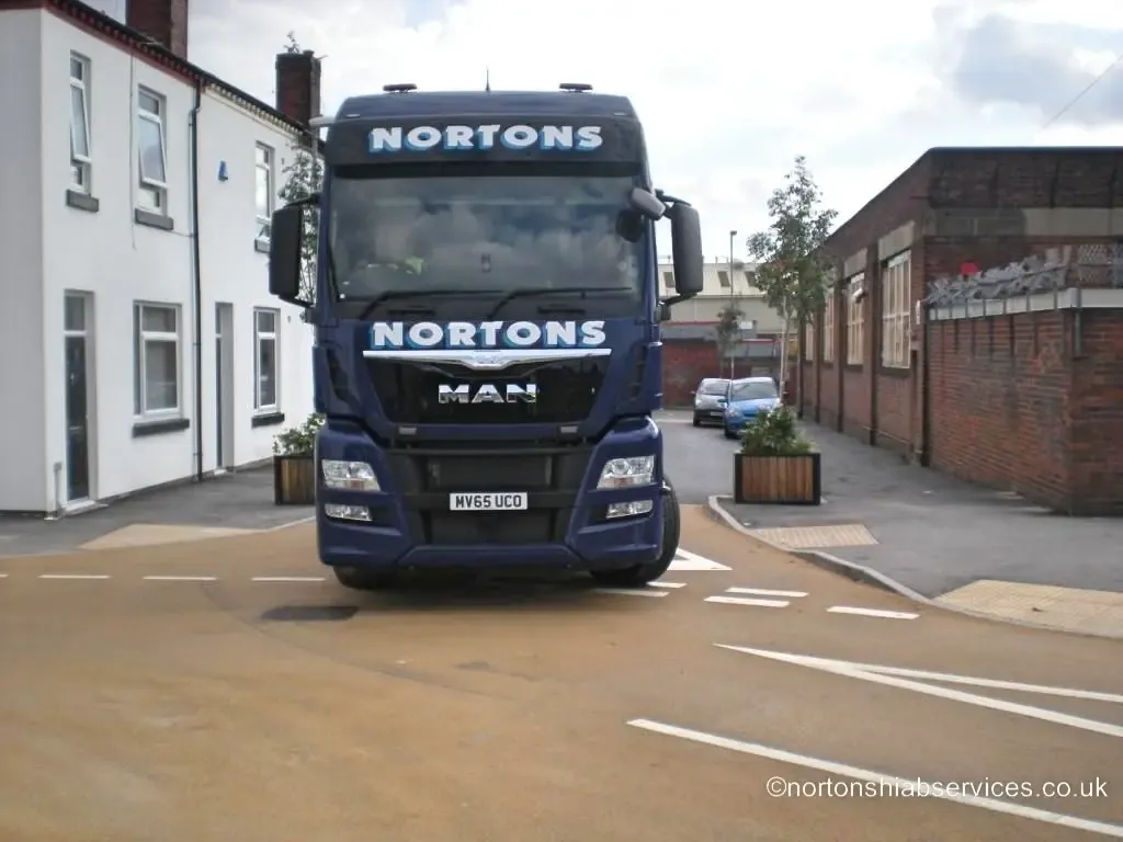 A Nortons MAN tractor unit on a newly finished residential street of white houses