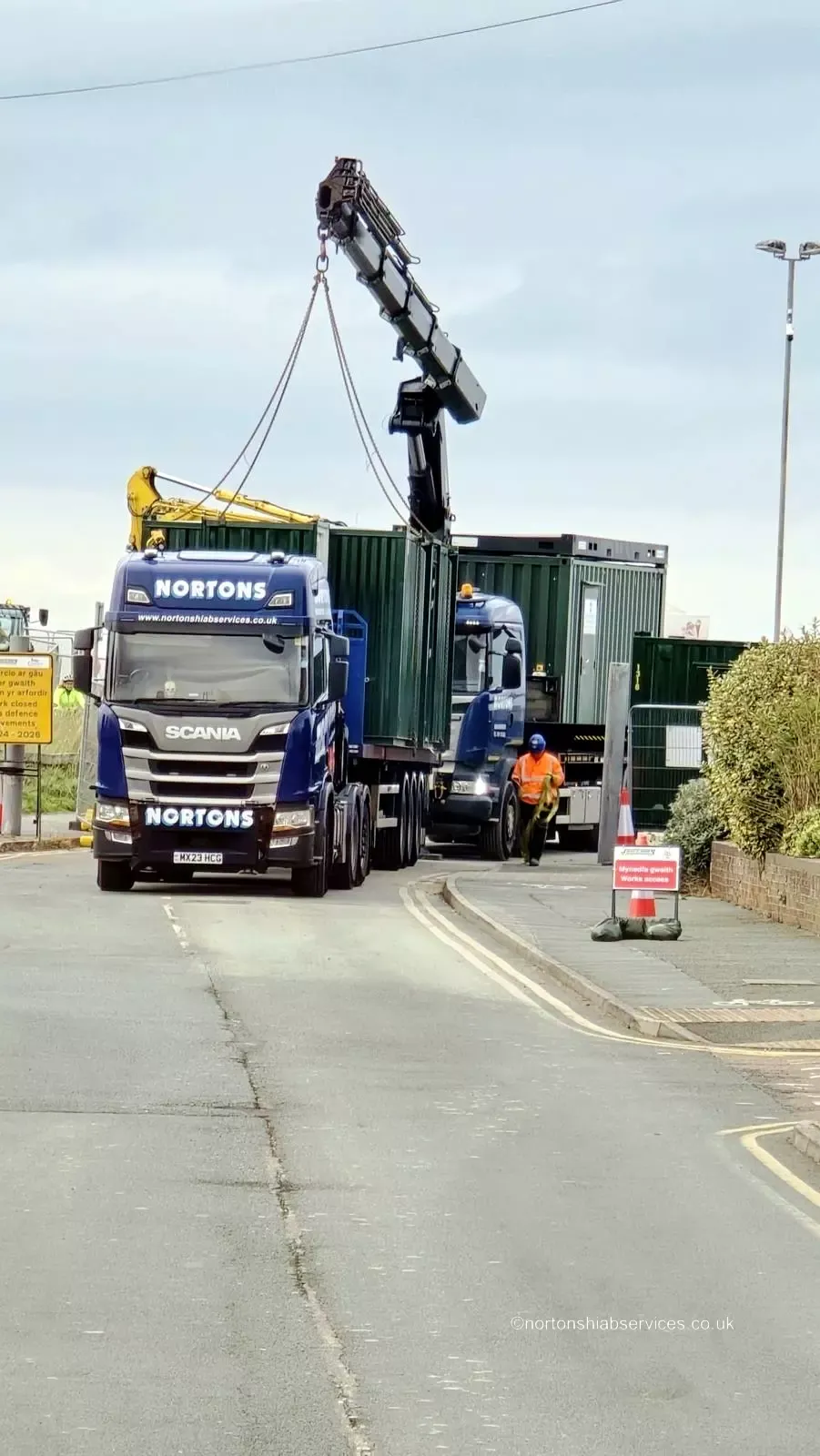 A Nortons Scania rigid with crane extended lifting a container on a city street