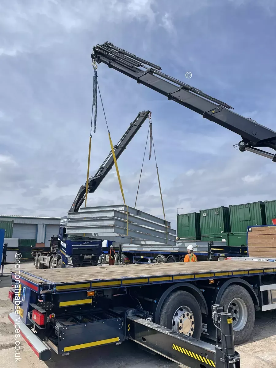 Two Nortons lorry cranes rigged either side of a long load on a construction site
