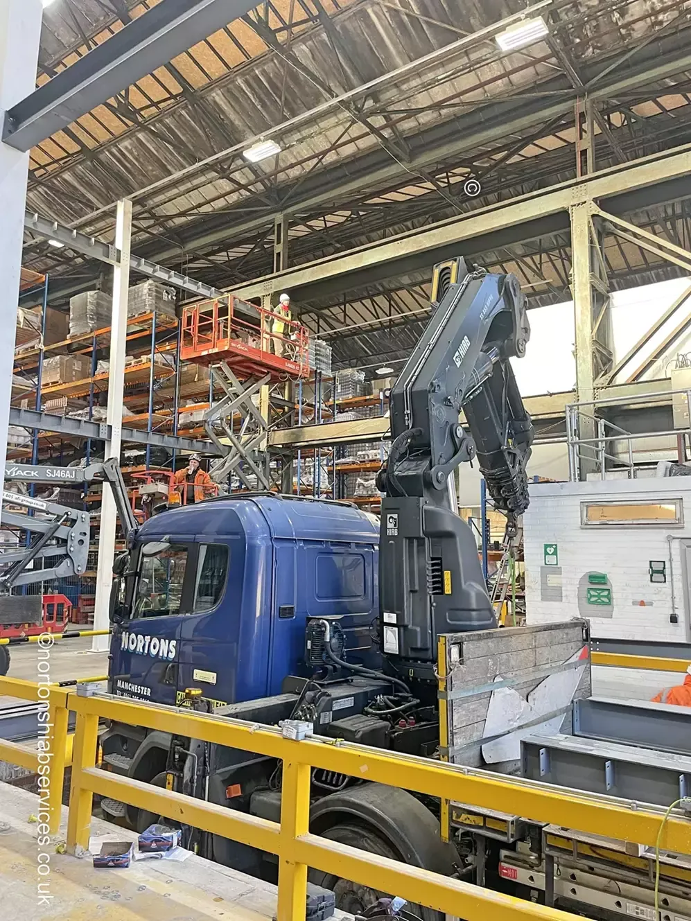 A Nortons Volvo rigid working inside a steel-framed warehouse with a crane extended