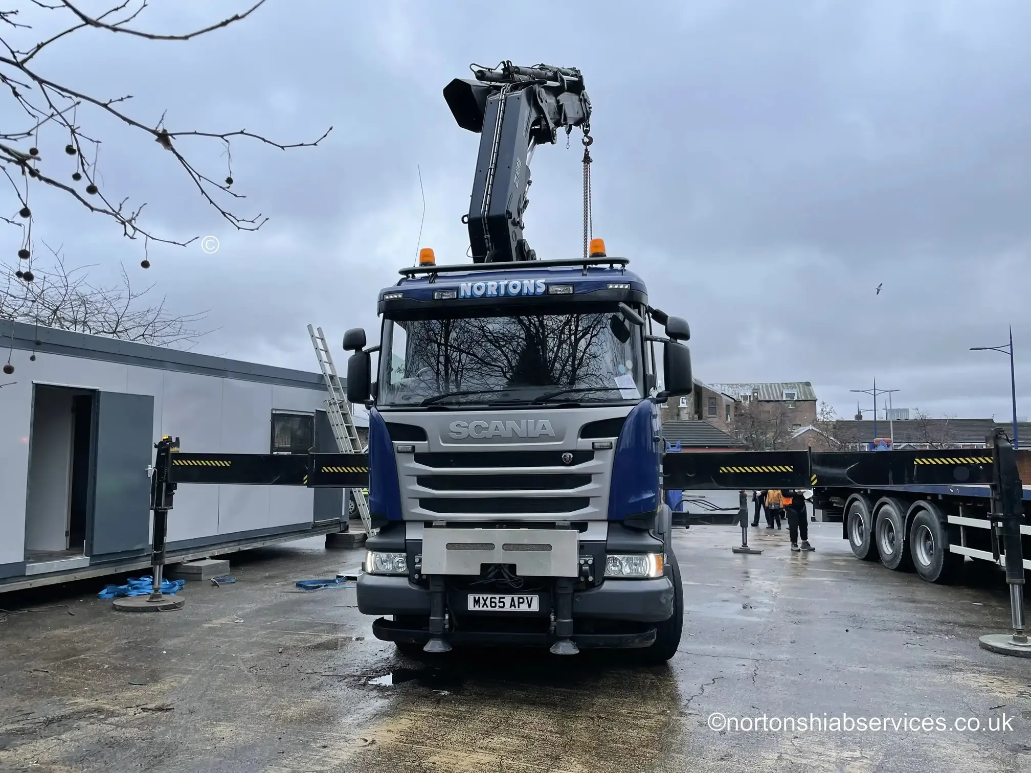 A Nortons Scania rigid with crane extended beside a modular school building under installation