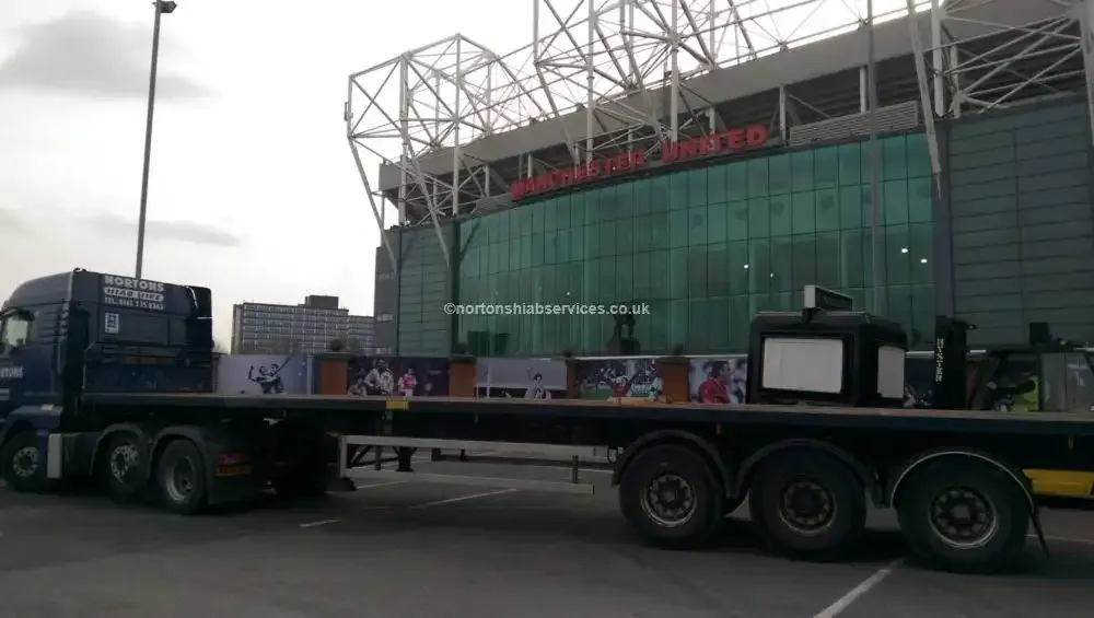 A Nortons flatbed trailer parked outside a large football stadium at dusk