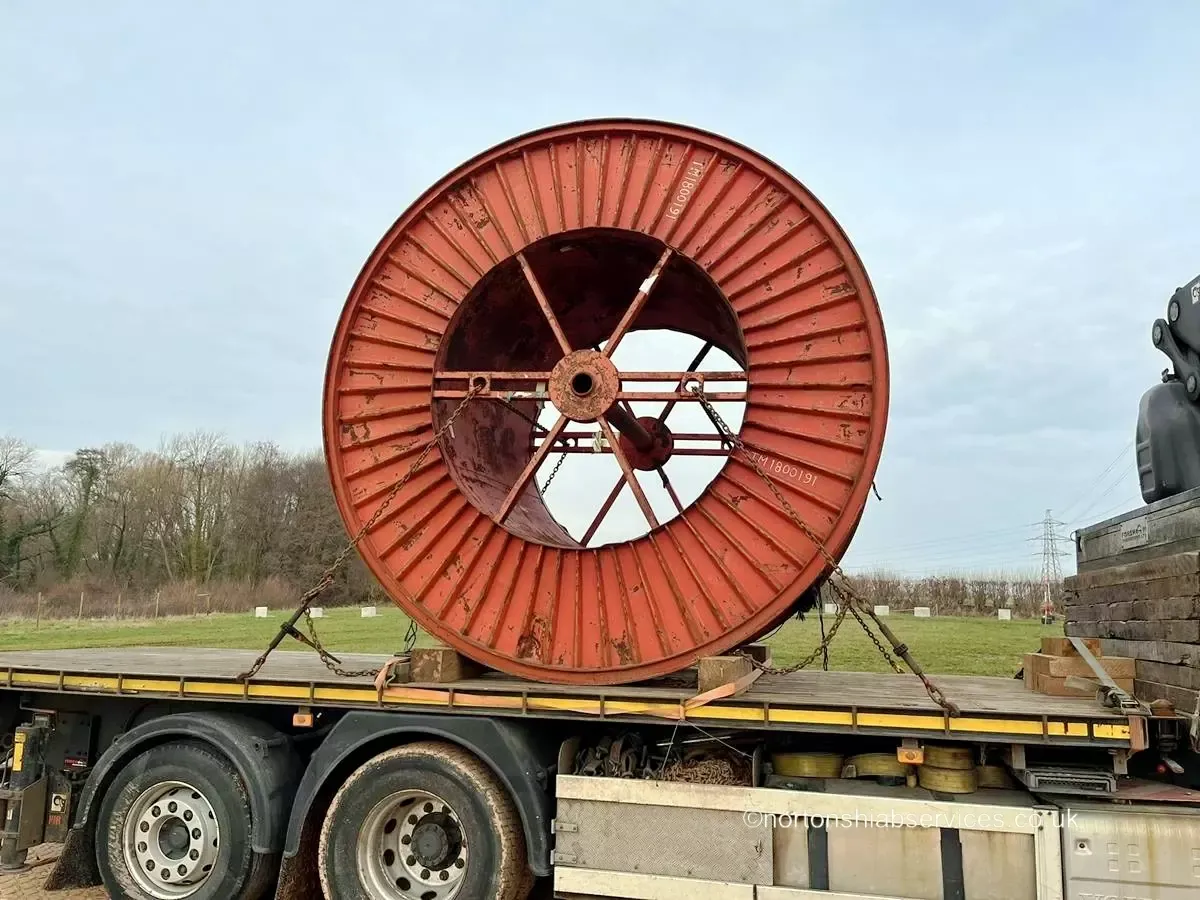A large red steel cable drum chained down on the bed of a Nortons flat trailer