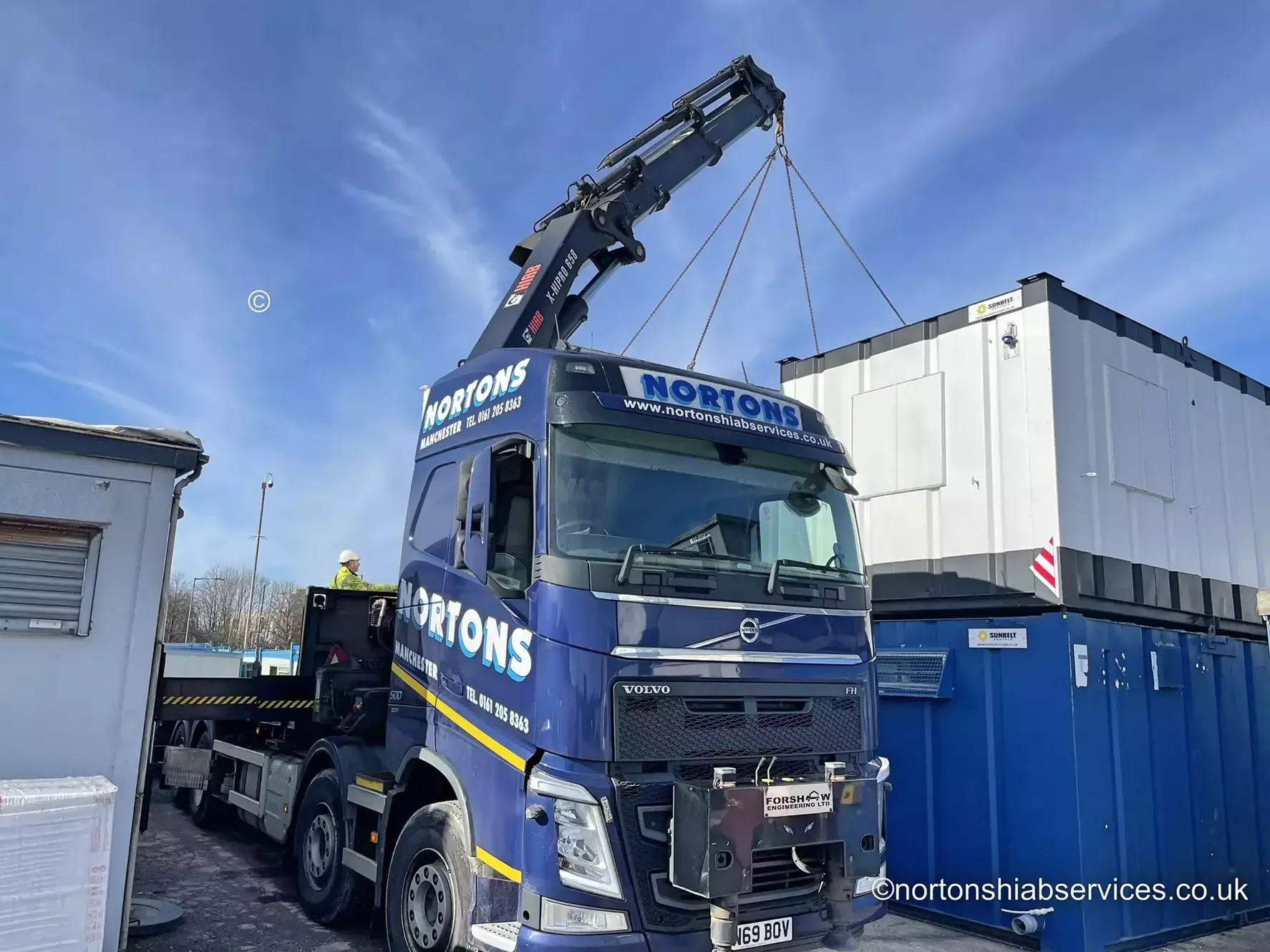 A Nortons Volvo rigid lifting a portable cabin on a bright day with blue sky behind