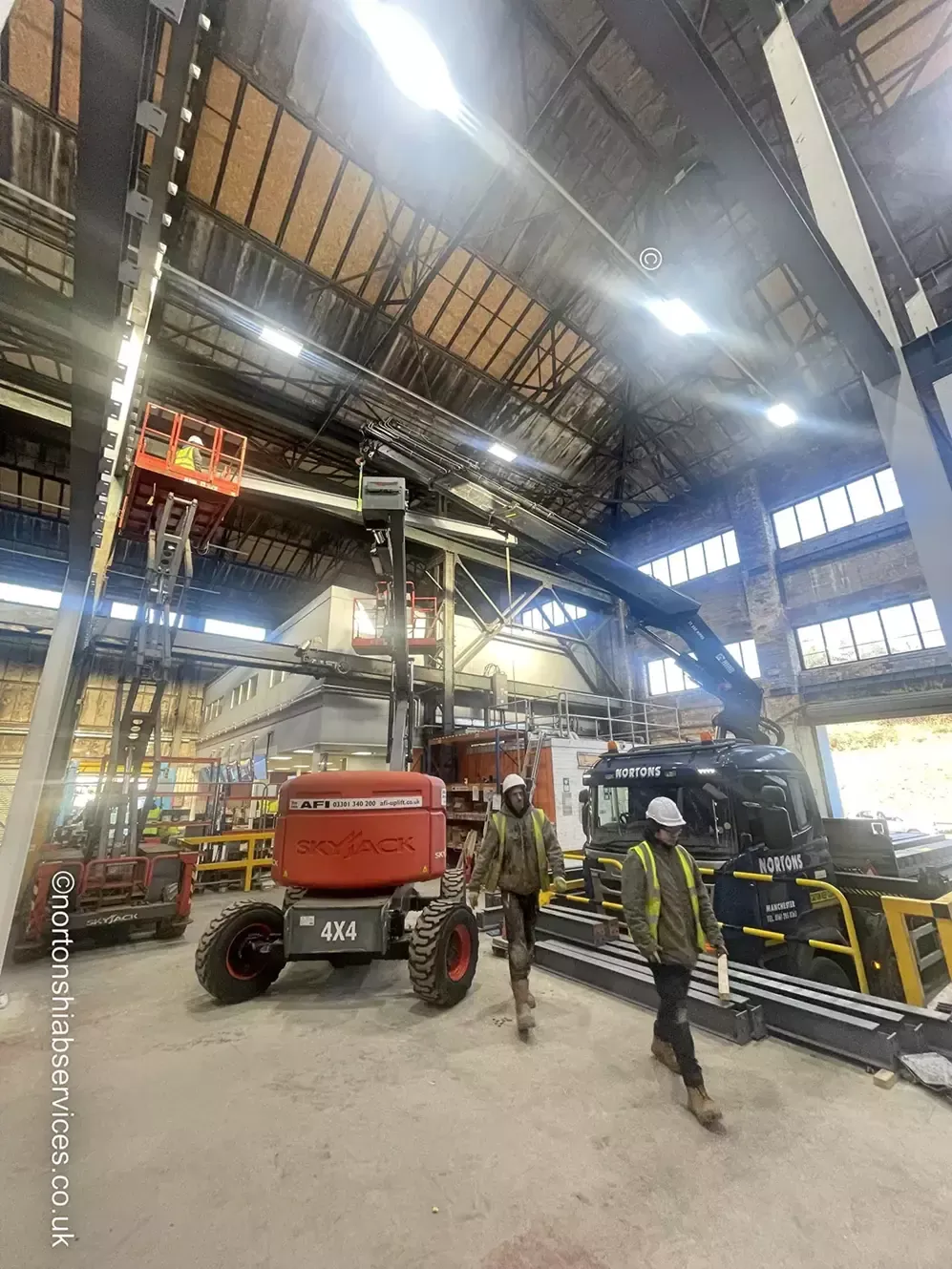 Site operatives and a Nortons crane working inside a warehouse with a cherry picker alongside