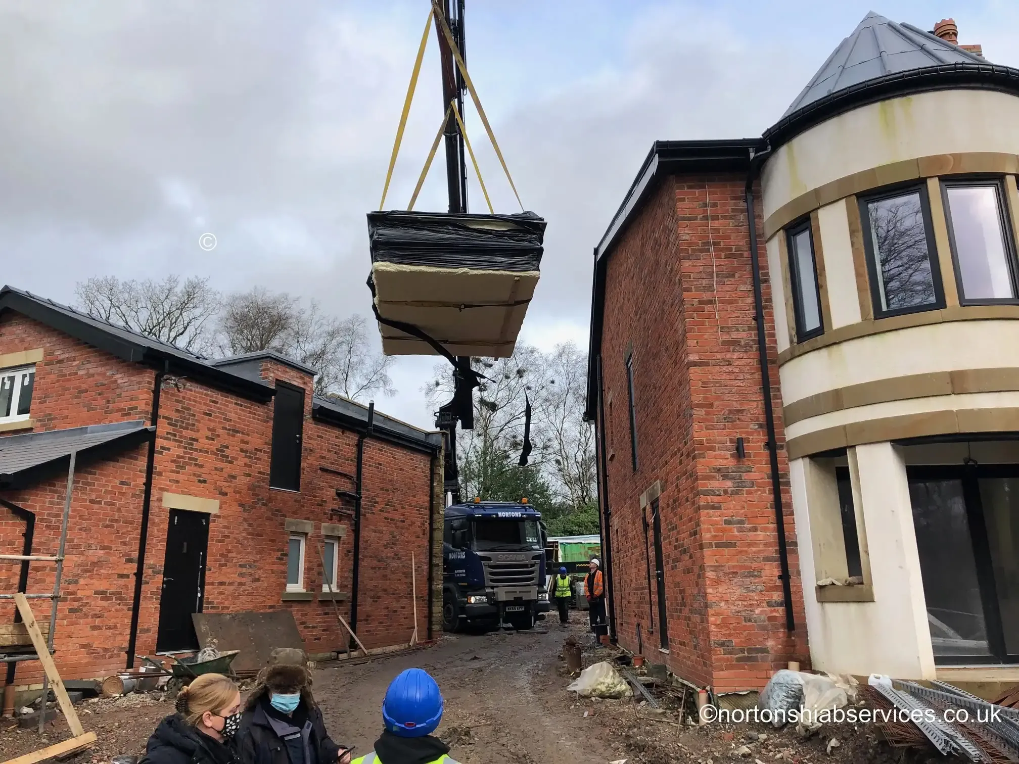 Nortons hiab lifting a wide unit between two buildings on a Wigan street
