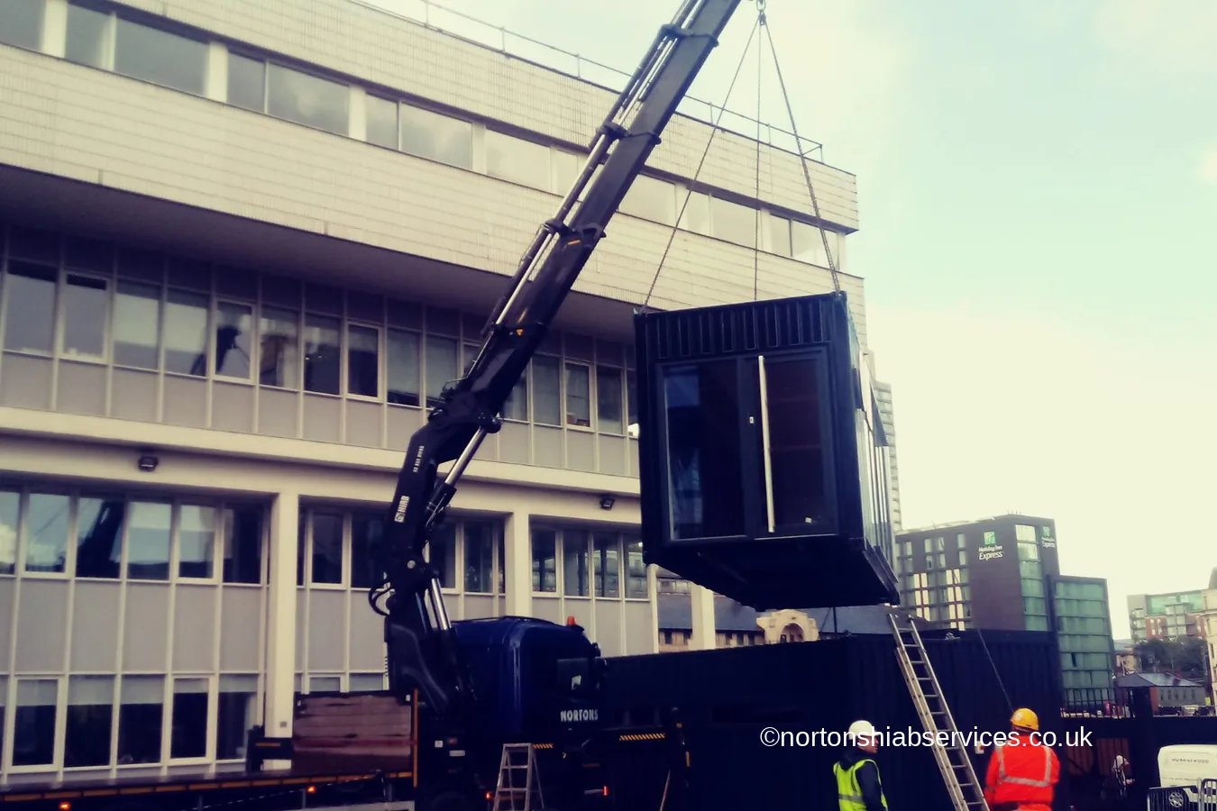 A Nortons crane lifting a dark modular studio unit at Circle Square in Manchester