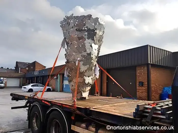 A tall openwork metal sculpture standing strapped upright on a Nortons flatbed