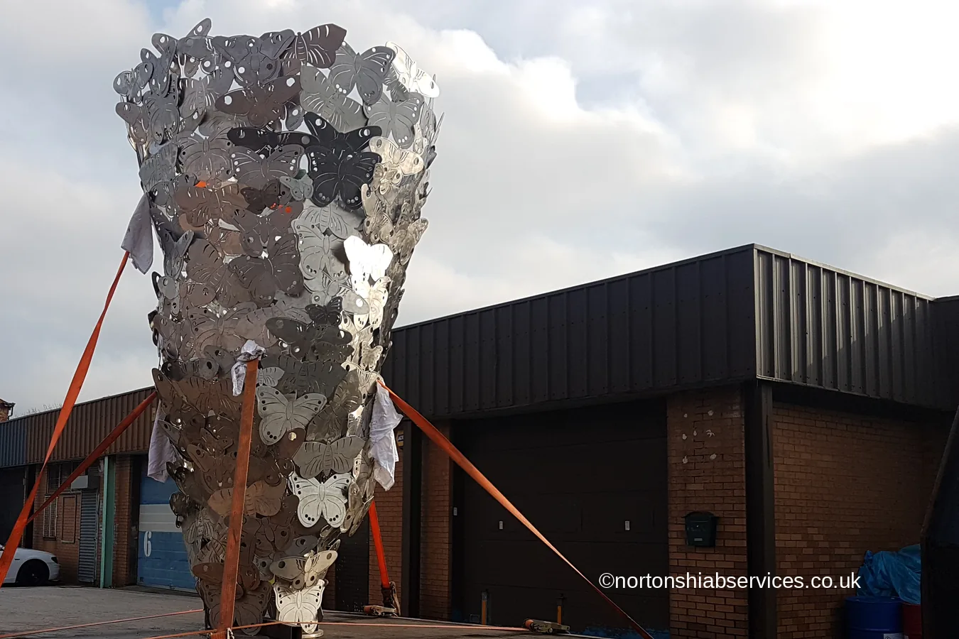 A tall openwork steel butterfly sculpture strapped upright on a Nortons flatbed