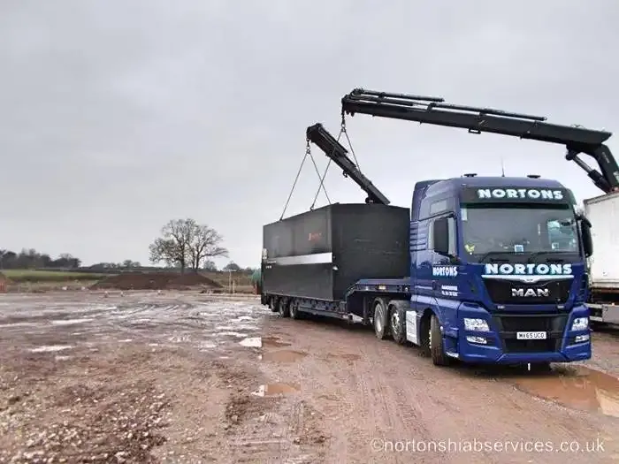 A Nortons MAN tractor unit and drawbar trailer carrying a long tank across an unmade site