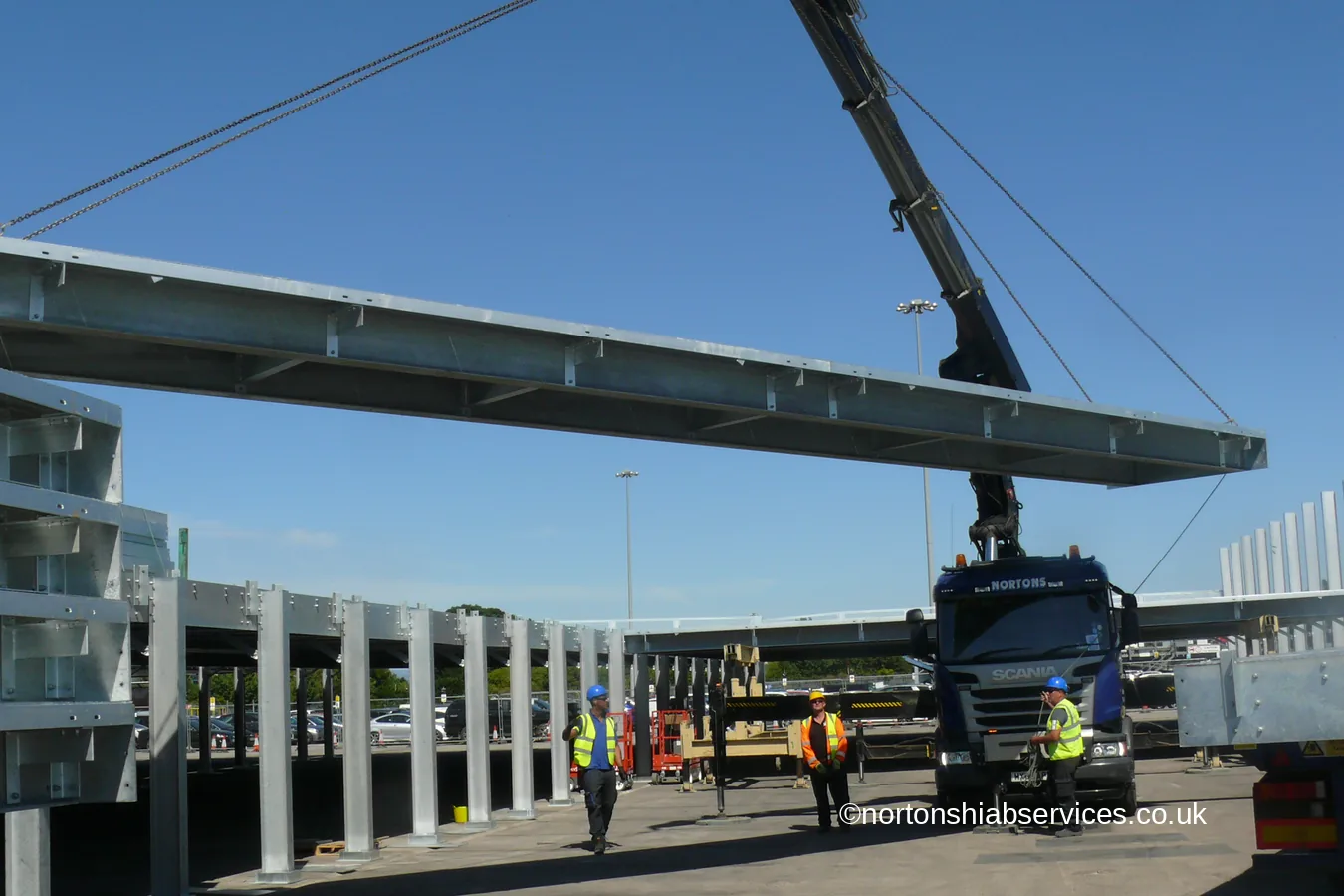 A Nortons hiab lifting a long galvanised steel beam on slings at Manchester Airport