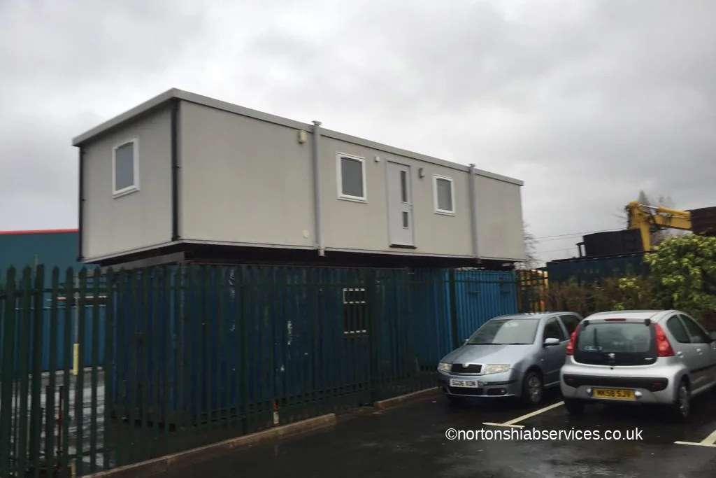 A forty by twelve foot modular site office set down inside a fenced yard at Bolton