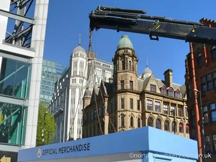 A Nortons crane lifting a unit between a modern glass frontage and Victorian stone buildings