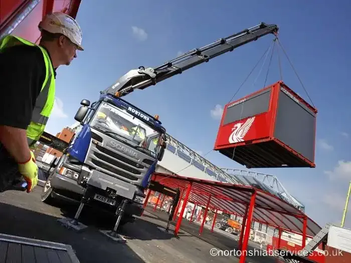 A Nortons crane lifting a red container at Anfield with the stand behind