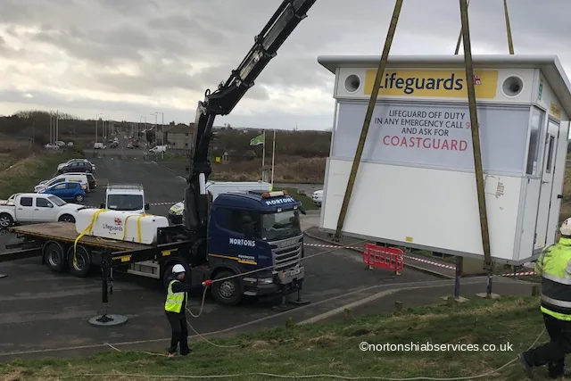 A Nortons crane lifting an RNLI lifeguard station on strops beside the coast