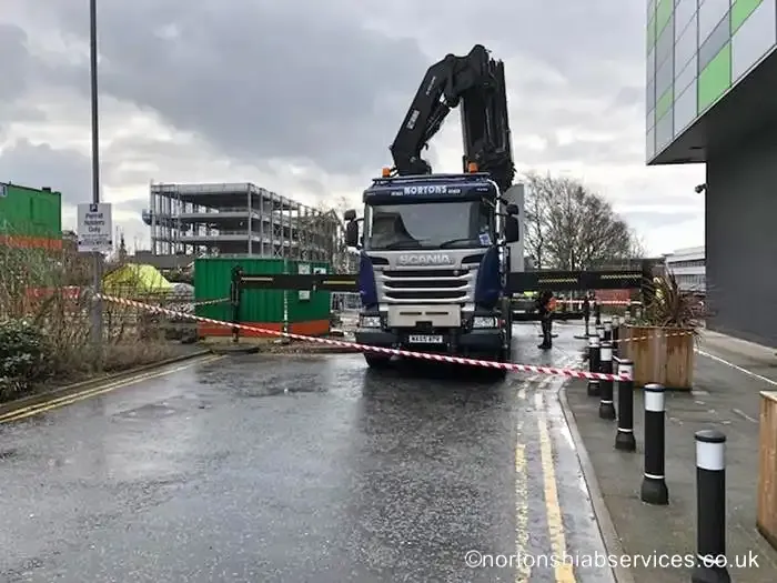 A Nortons hiab set up on its stabiliser legs in a wet street closed off with hazard tape