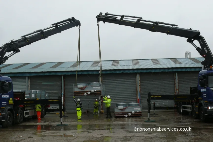 Two Nortons lorry cranes lifting one load between them outside a goods warehouse