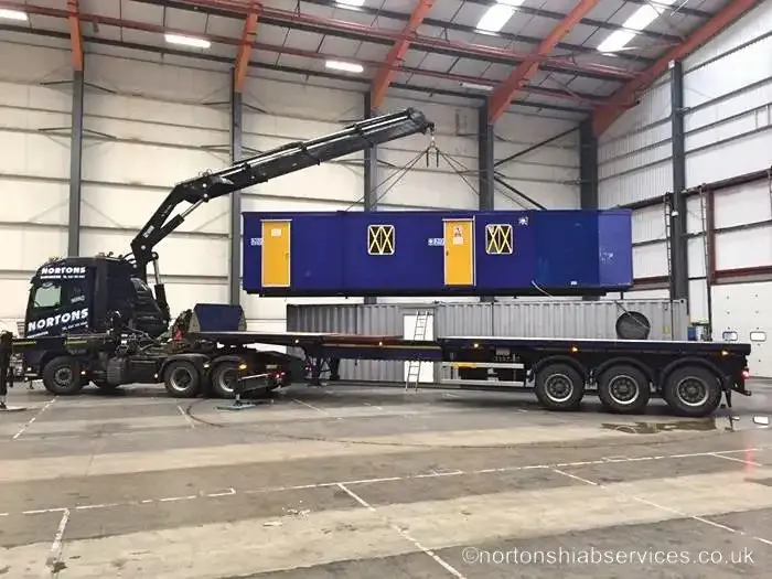 A blue welfare unit being loaded onto a Nortons trailer inside a warehouse