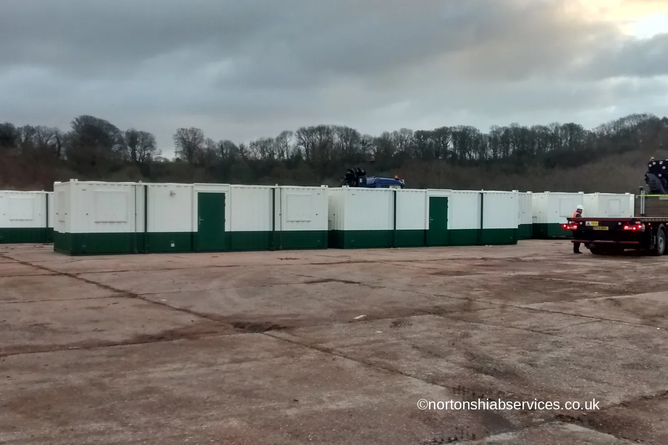 A long run of green and white welfare cabins set out across a yard at Caernarfon by Nortons