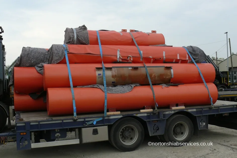 Large orange cylindrical speaker housings strapped on a Nortons flatbed after a festival