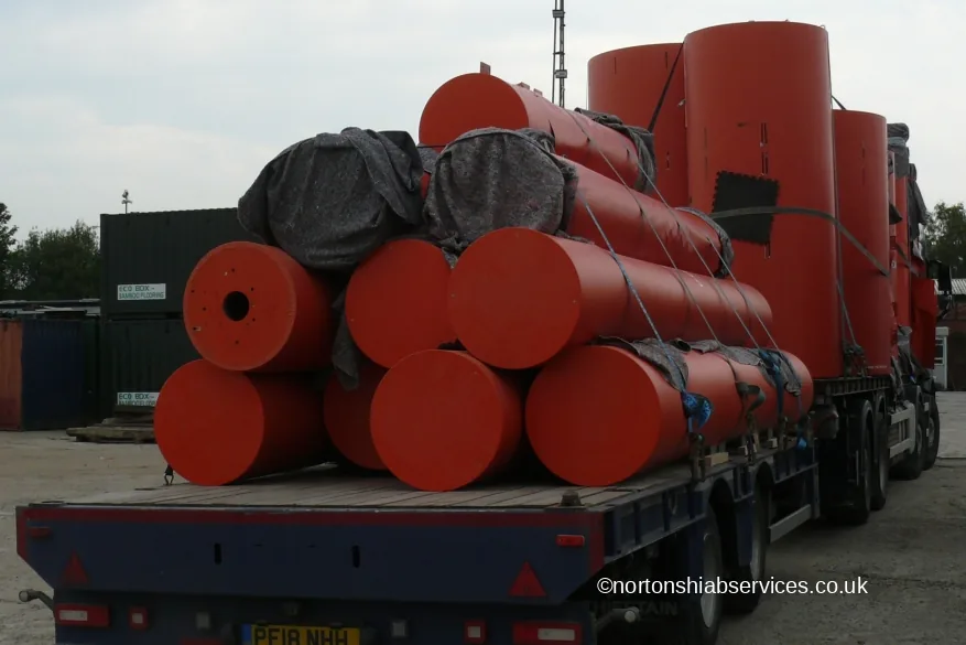 Orange cylindrical speaker housings stacked in layers and roped down on a Nortons trailer