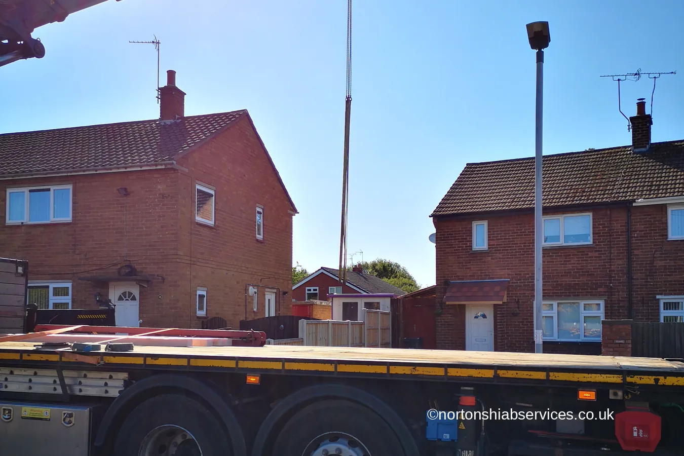 A Nortons hiab set up on its stabiliser legs in a residential street with the boom raised