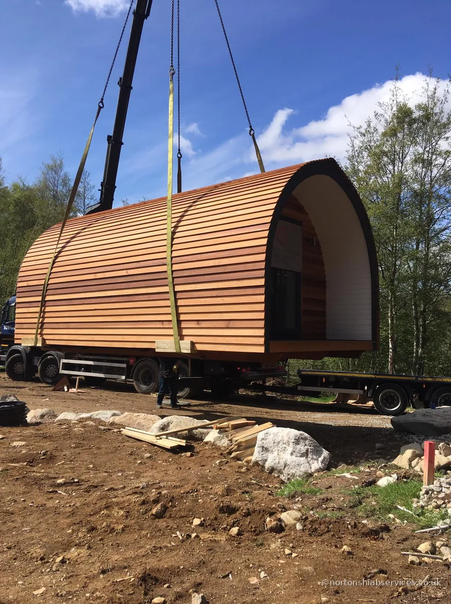A Nortons crane lifting a cedar glamping pod clear of the trailer over a stone base