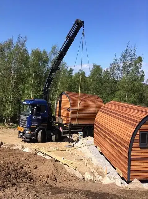 A Nortons lorry crane lowering a glamping pod onto its base beside one already in place