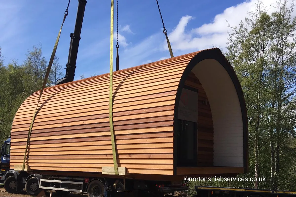 A cedar glamping pod suspended on strops above its prepared base
