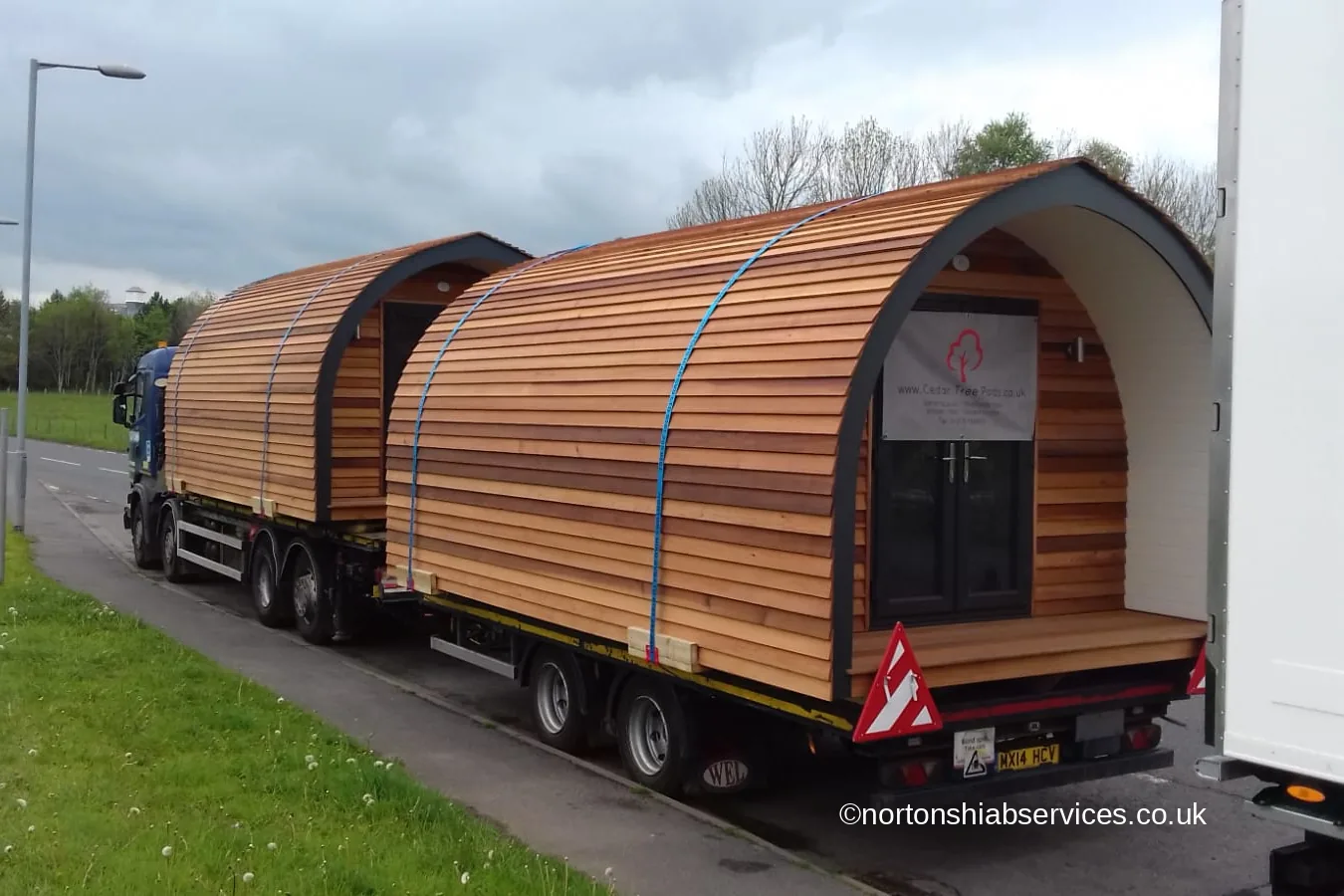 Two cedar glamping pods loaded nose to tail on a Nortons wagon and drag on a main road